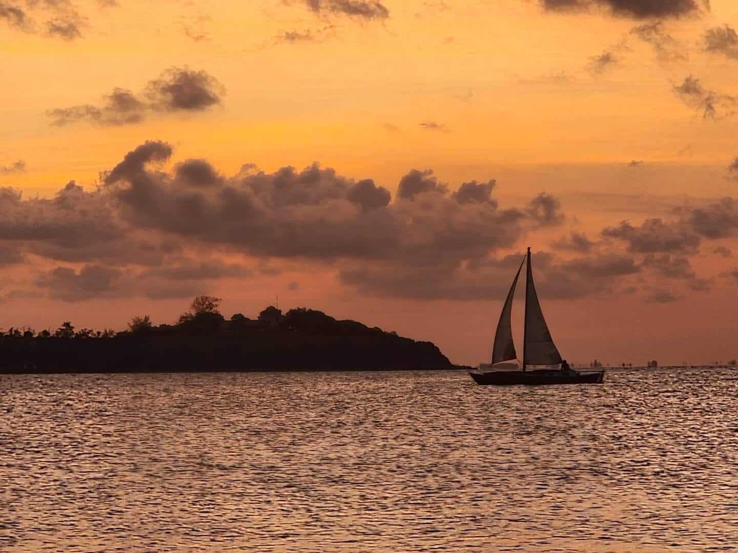 Veleiro passando na frente do pôr do sol, na lagoa em frente à casa